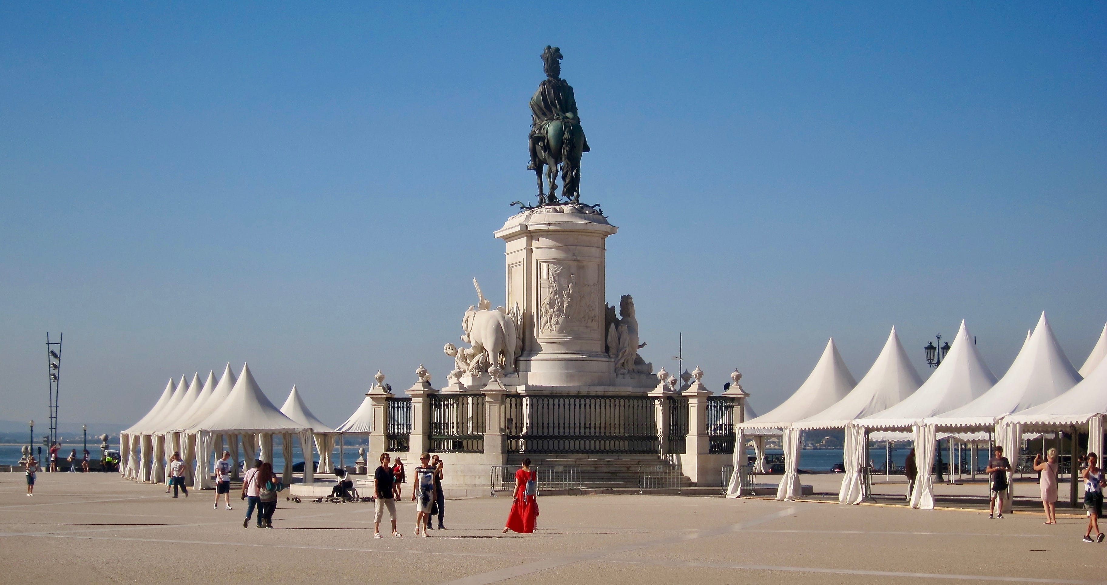 a large square with tented stalls. A woman in a red dress stands before the statue at its center