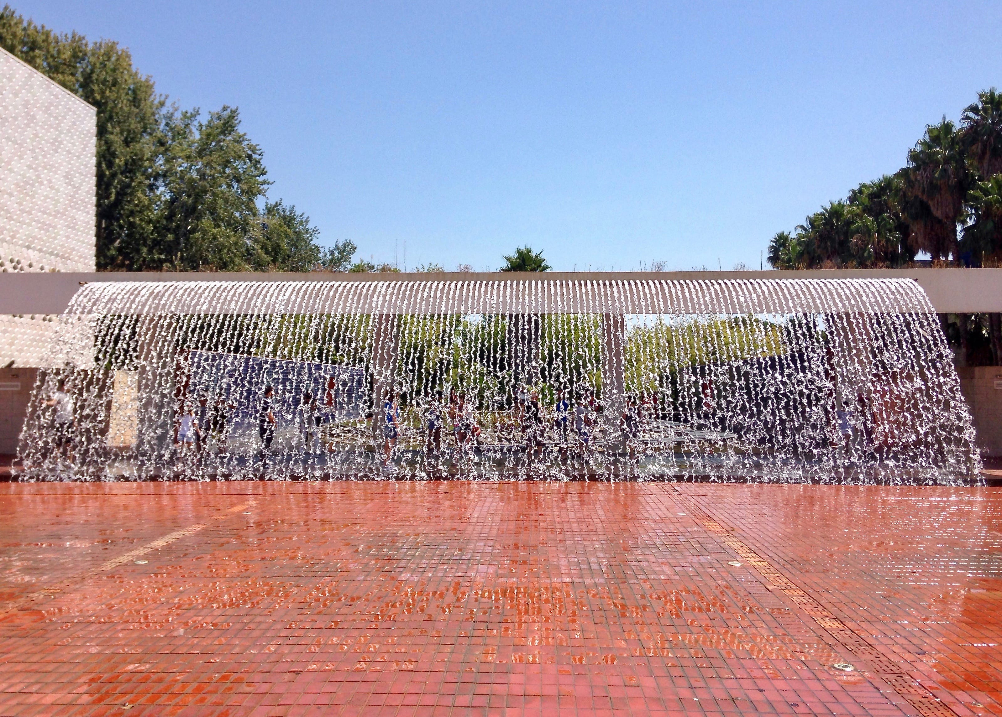 a very wide waterfall-like fountain fronting a red brick square