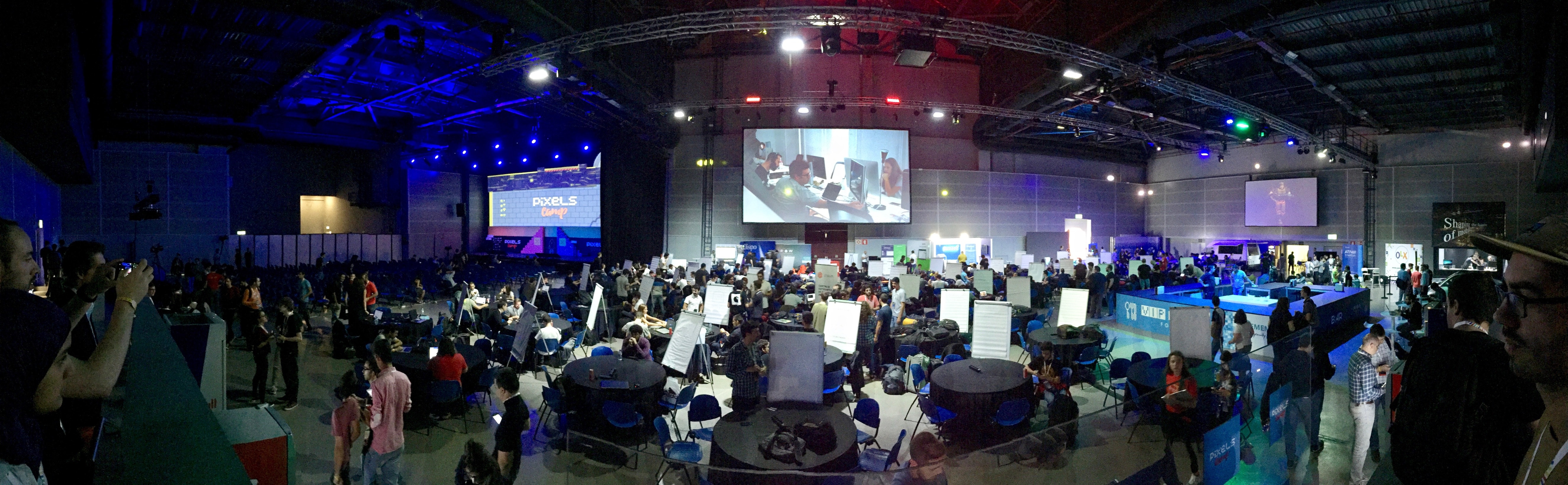 hundreds of tables and people inside a large pavilion. A stage can be seen to the left.