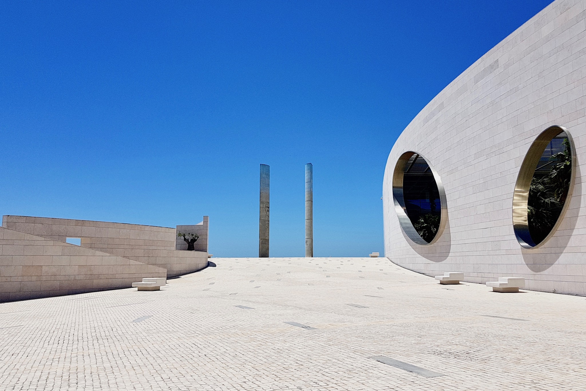 a wide plaza between curved buildings with oval openings