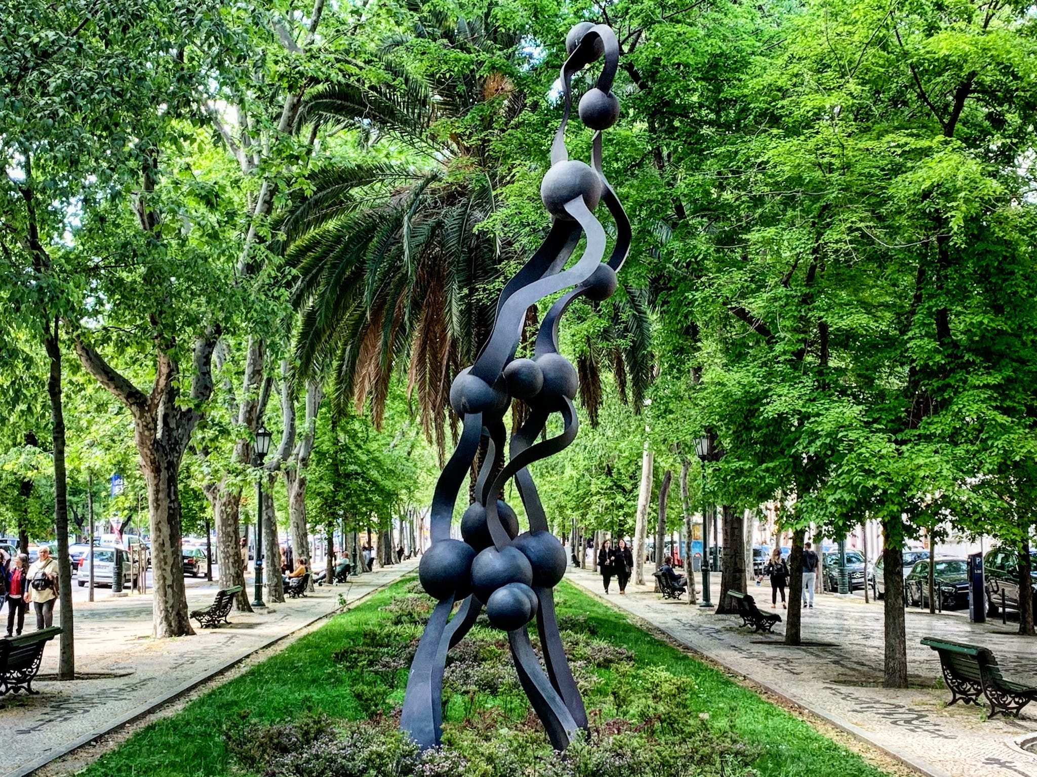 a modern bronze statue amidst a garden avenue